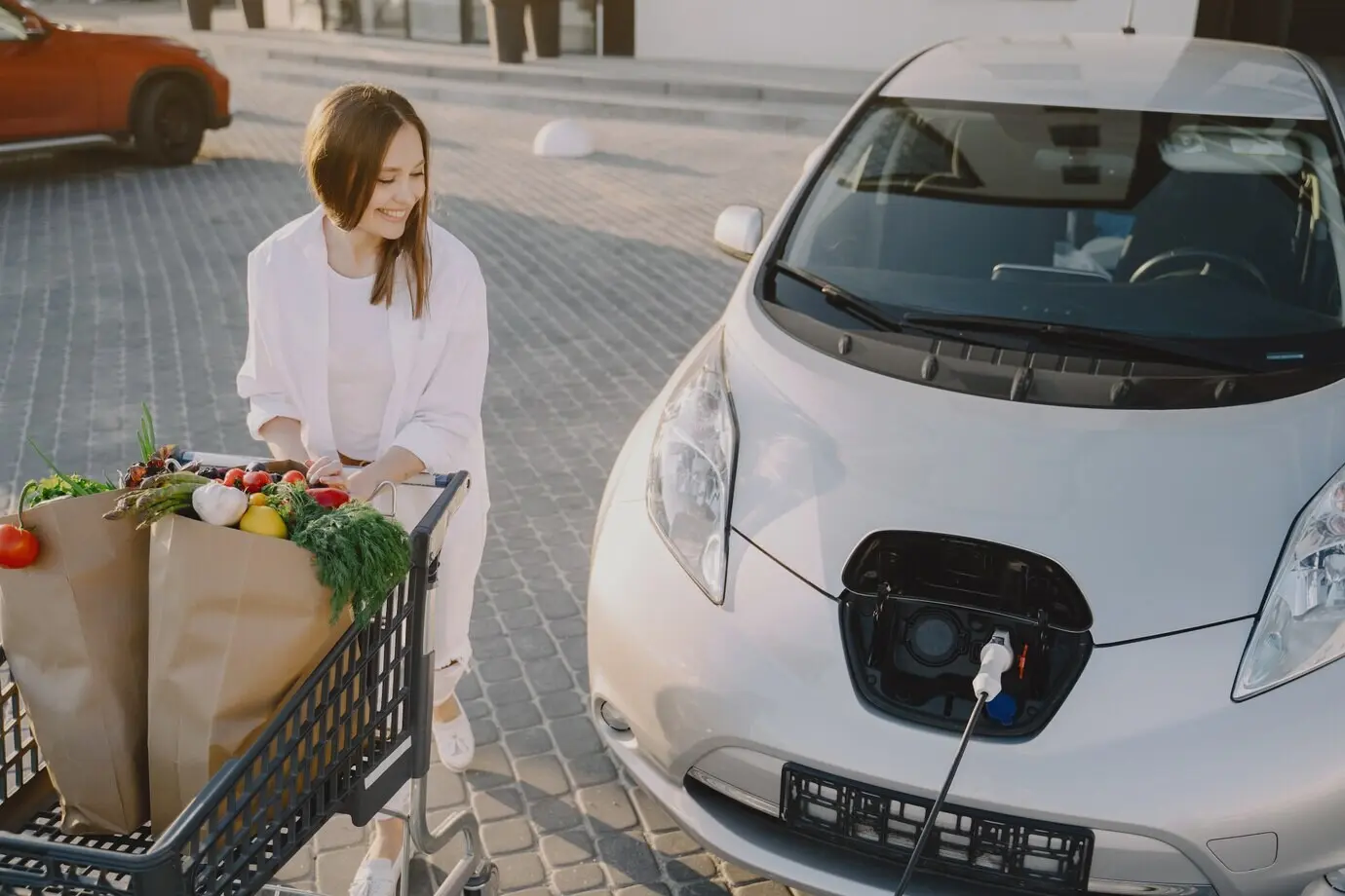 A woman with a shopping cart next to her car.