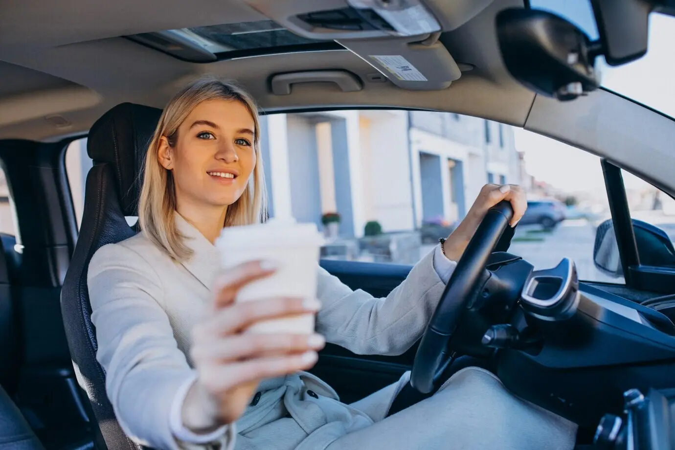 A woman sits inside an electric car while it charges, with a coffee cup.